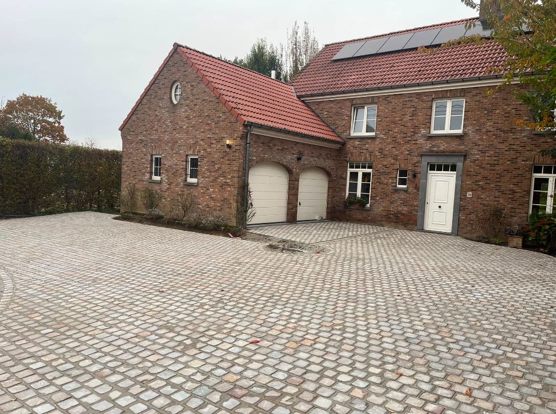 Grande cour en pavés devant une maison en briques avec un garage double